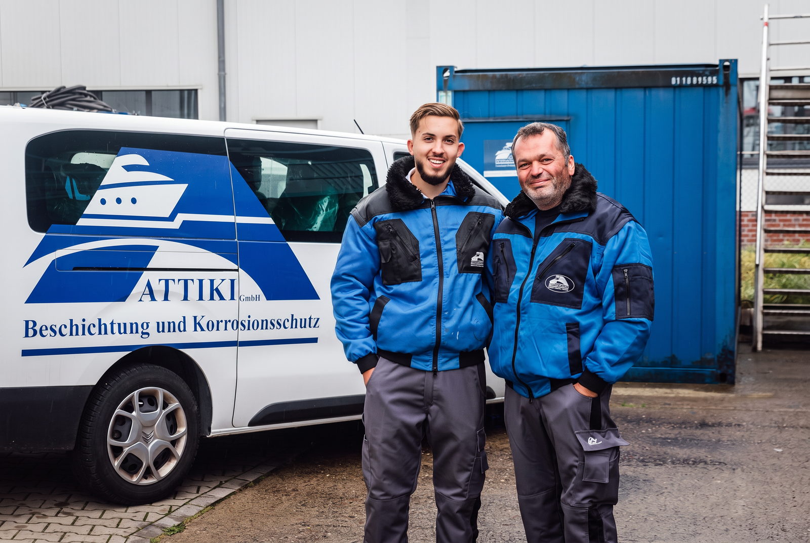 Zwei ATTIKI-Mitarbeiter in Arbeitskleidung vor einem Firmenfahrzeug am Betriebsgelände in Bremen